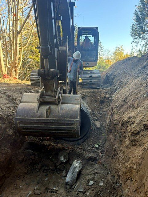 Excavator bucket setting culvert pipe in a rock trench