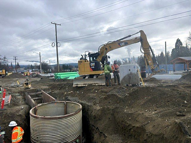 CAT excavator setting a CSP manhole with PVC pipe staged
