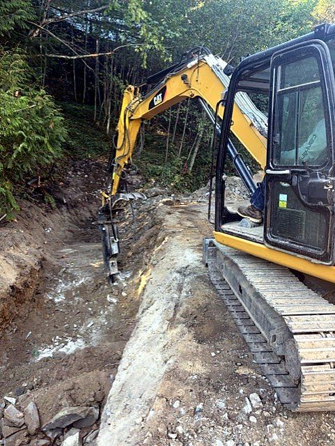 Mini excavator with hammer attachment trenching through rock