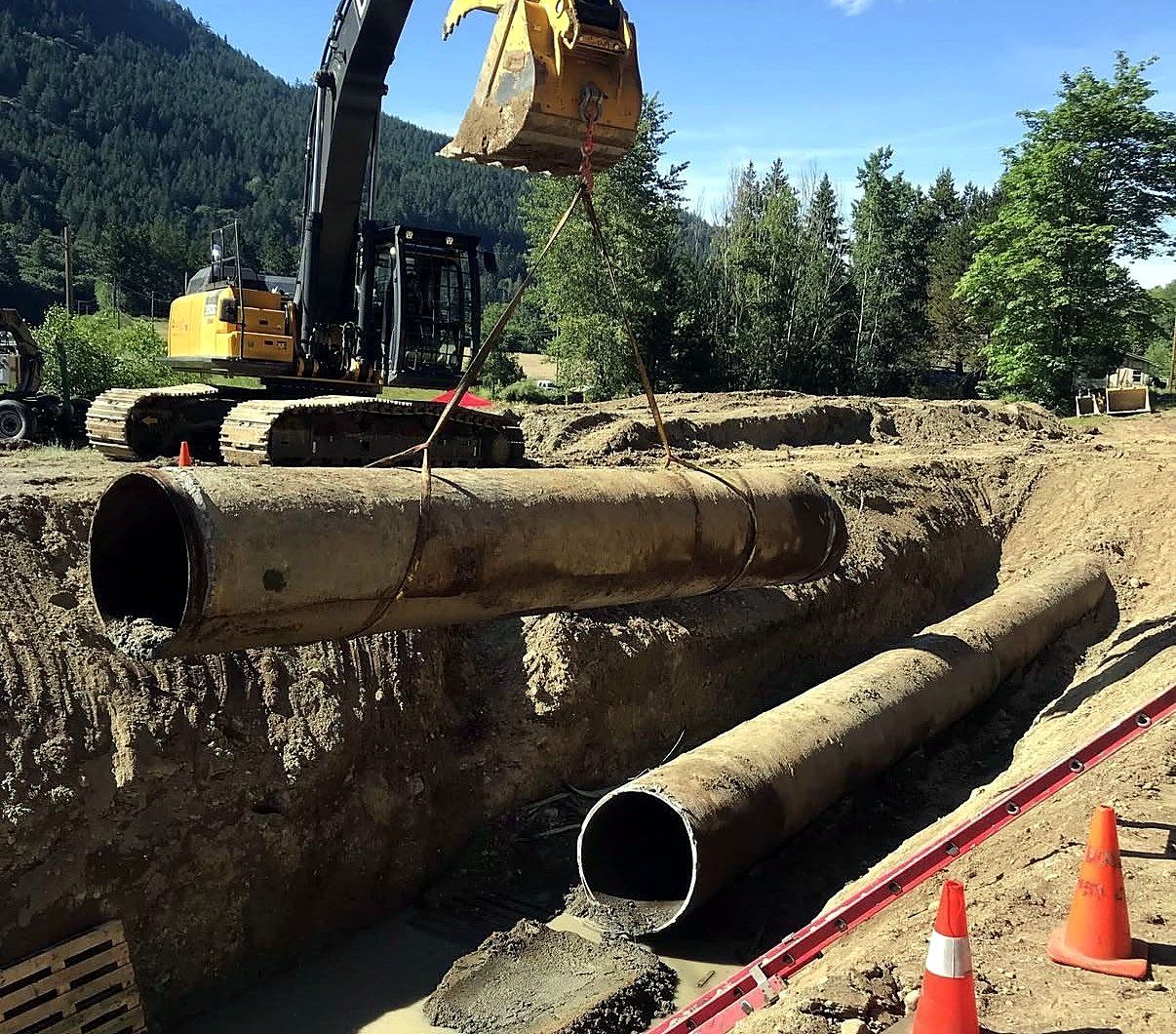 Step 3, remove: excavator lifting a cut section of pipe out of the trench
